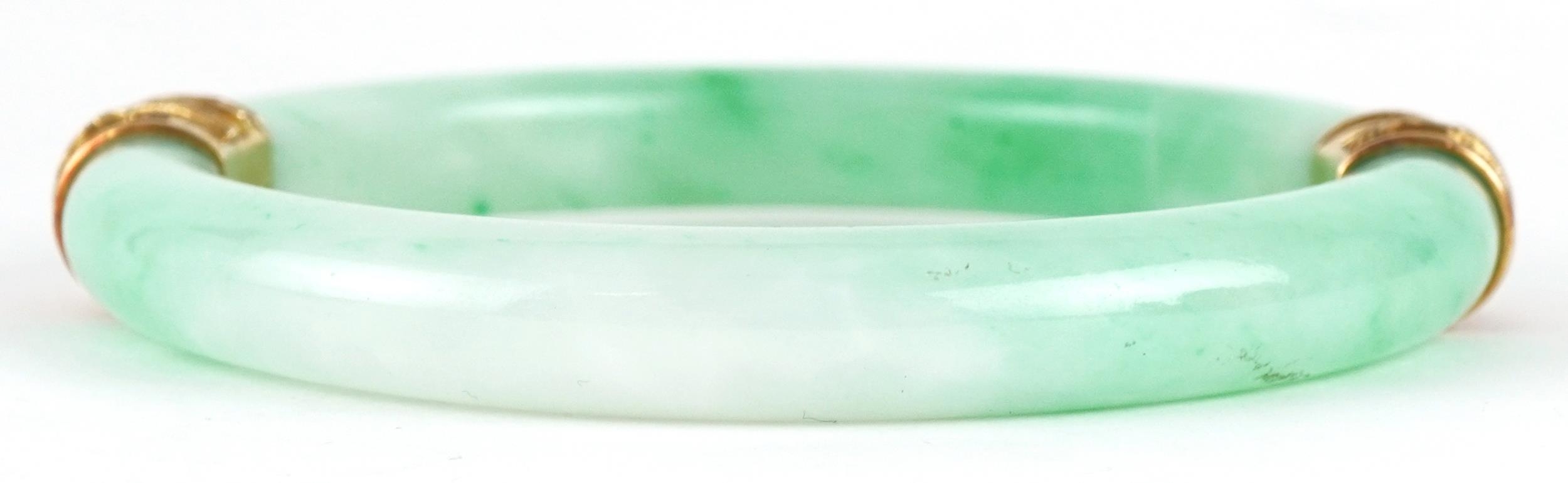 Chinese green jade bangle with unmarked gold mounts decorated in relief with dragons, 9.5cm in