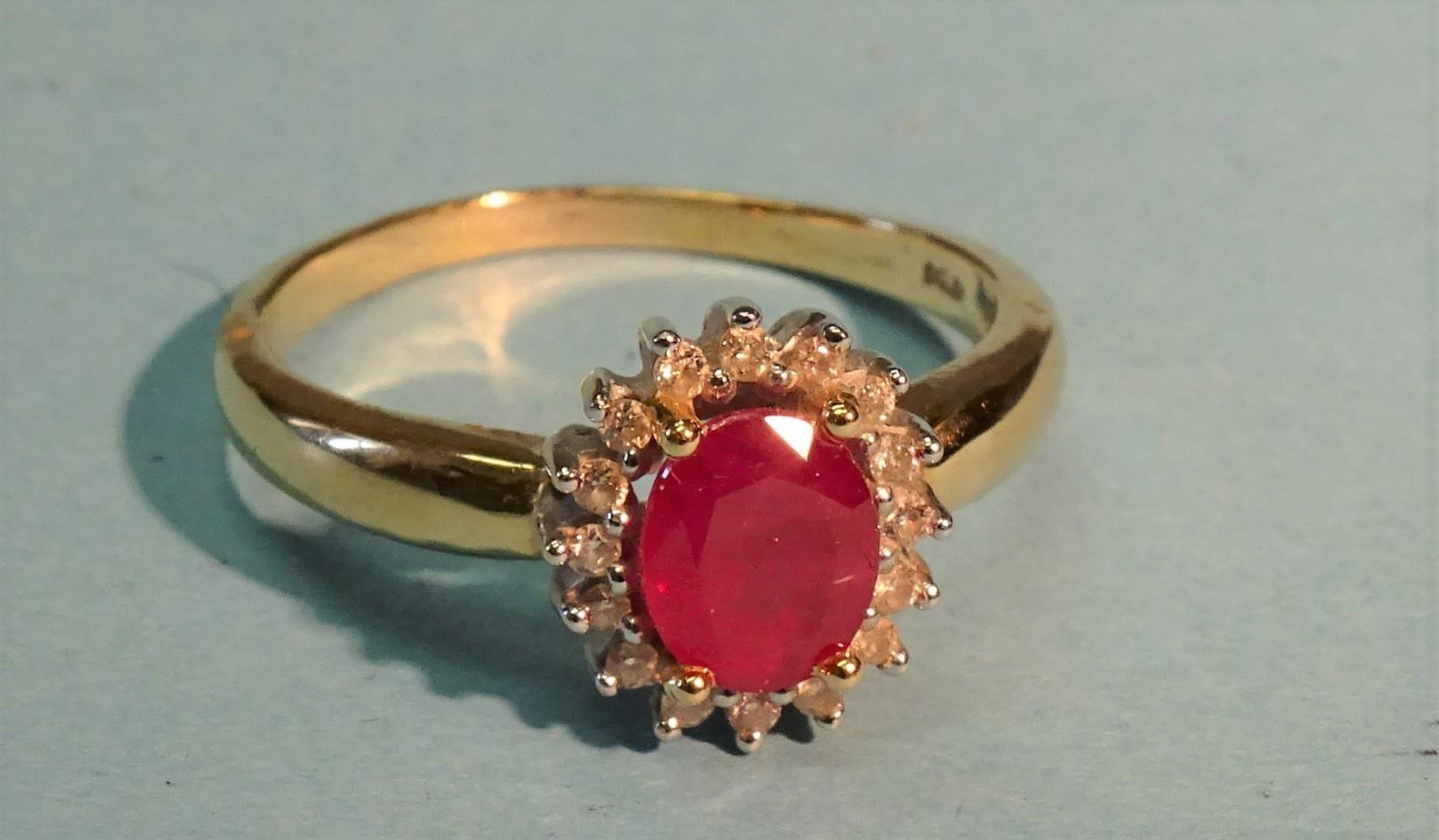 A ruby and diamond cluster ring claw-set an oval ruby within a surround of sixteen diamond points,