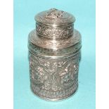 An Asian white metal tea cannister with embossed decoration of figures in cartouches and temple