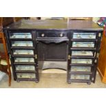 An unusual Edwardian ebonised kneehole cabinet of drawers, the central drawer flanked by twelve