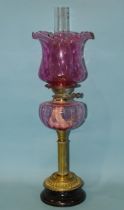 A late-19th century oil lamp, the cranberry glass reservoir on brass reeded column and circular