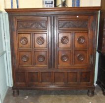 A large antique oak two-door food cupboard, with later cornice above a pair of carved panelled