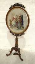 A William IV rosewood tripod fire screen with oval needlework panel depicting two figures seated