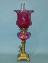 A late-19th century oil lamp, the cranberry glass reservoir on brass reeded column with applied