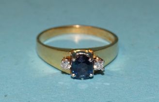 A sapphire and diamond ring claw-set an oval sapphire between two brilliant-cut diamonds, in 18ct