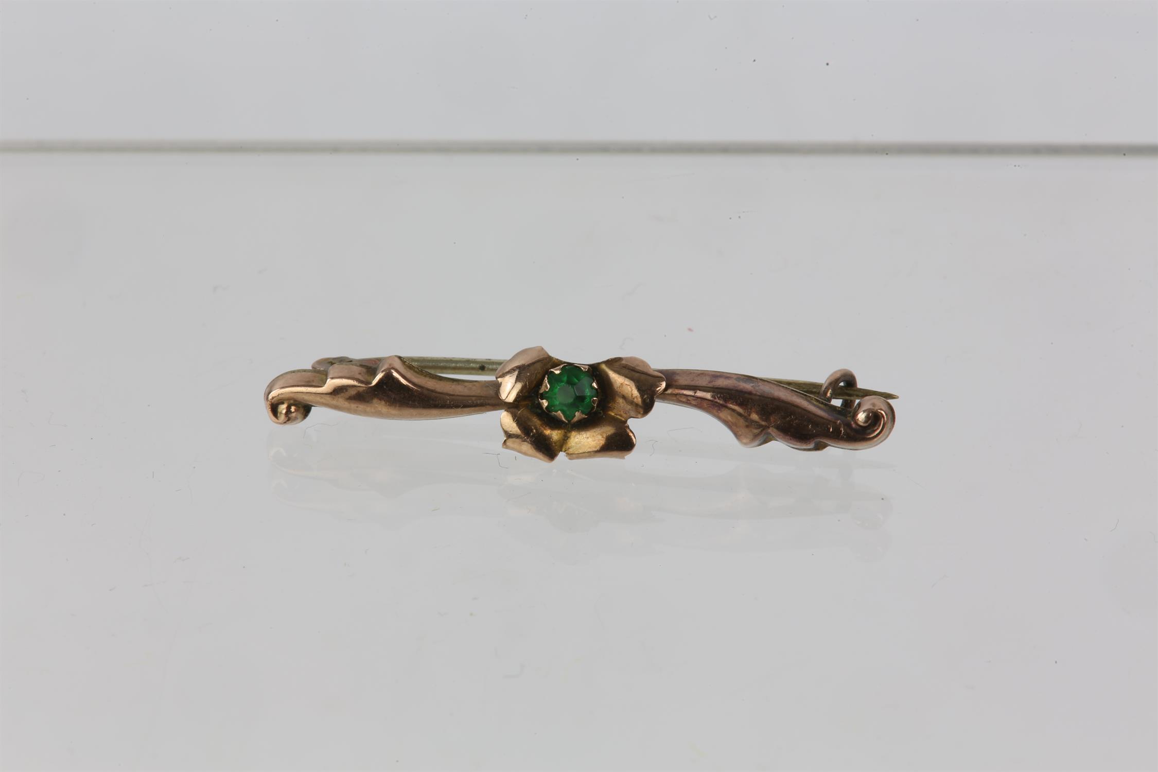 Floral bar brooch set with a green paste stone, set in yellow meta; with a partial 9ct stamp,