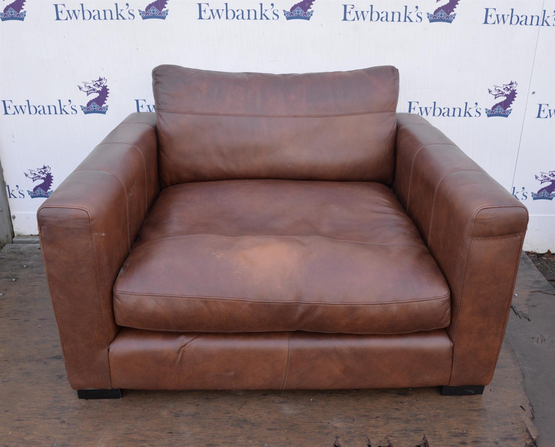 A large brown leather upholstered armchair raised on pad feet. 126 cm wide x 120 cm deep x 66 cm