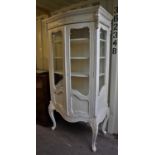 Continental style cream painted display cabinet, the foliate carved frieze over a pair of glazed