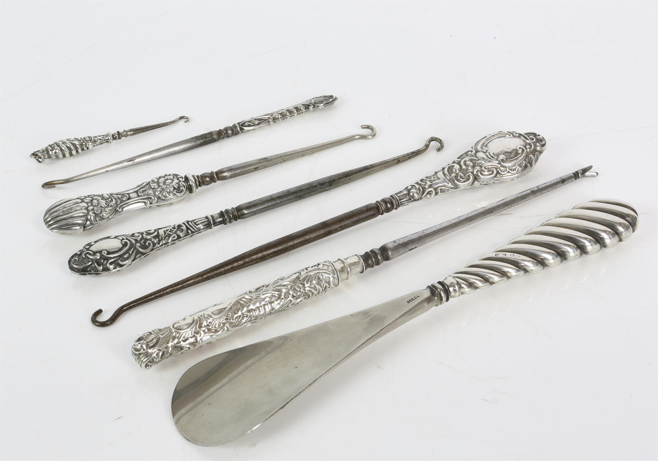 Seven silver handled tools including a shoe horn, and button hooks, varied designs and date