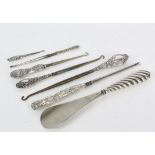 Seven silver handled tools including a shoe horn, and button hooks, varied designs and date