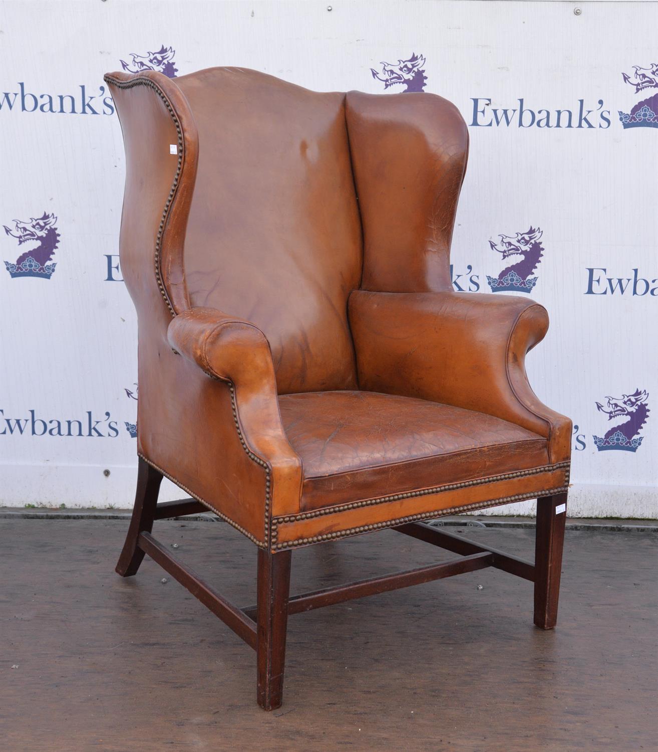 A brown leather upholstered wing back armchair raised on square supports joined by stretchers.