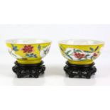 A pair of yellow ground, famille rose bowls; each one decorated with floral panels and peony heads.