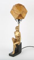 Art Deco gilt decorated and black painted plaster table lamp, the woman seated on a stepped base,
