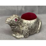 A silver plated camel pincushion with red stone eyes