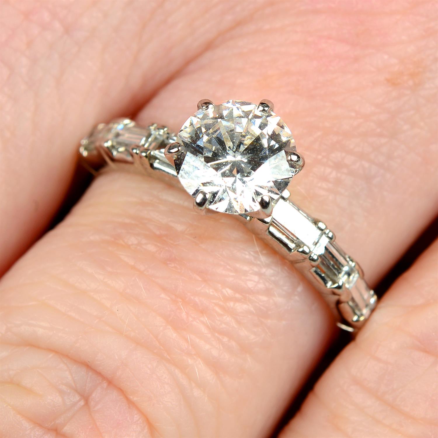 An 18ct gold brilliant-cut diamond single-stone ring, with rectangular-shape diamond shoulders.