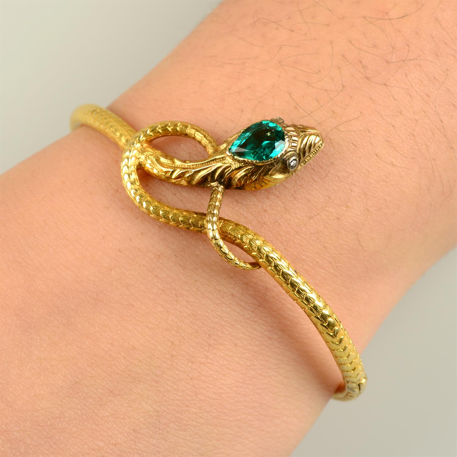An early 19th century 18ct gold engraved snake bangle, with Colombian emerald crest and diamond