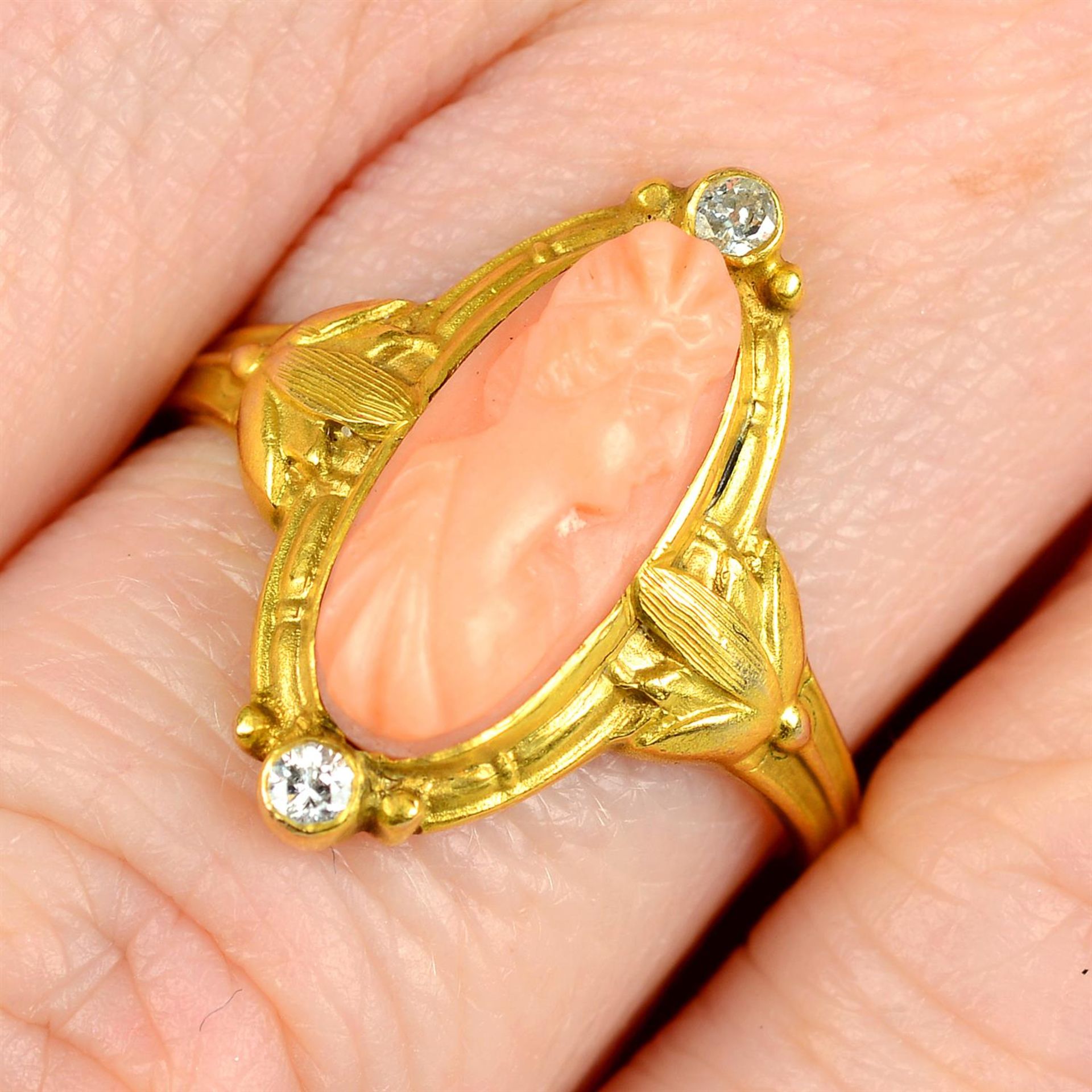 An early 20th century gold, coral cameo and circular-cut diamond ring, with foliate shoulders.
