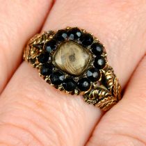 A Georgian gold black garnet mourning ring, with hairwork panel and foliate shoulders.