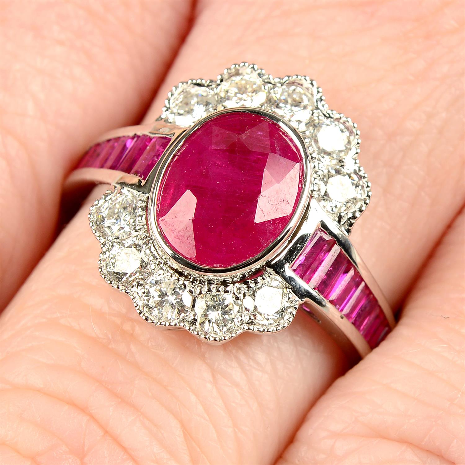 An 18ct gold oval-shape ruby and brilliant-cut diamond cluster ring, with calibre-cut ruby line