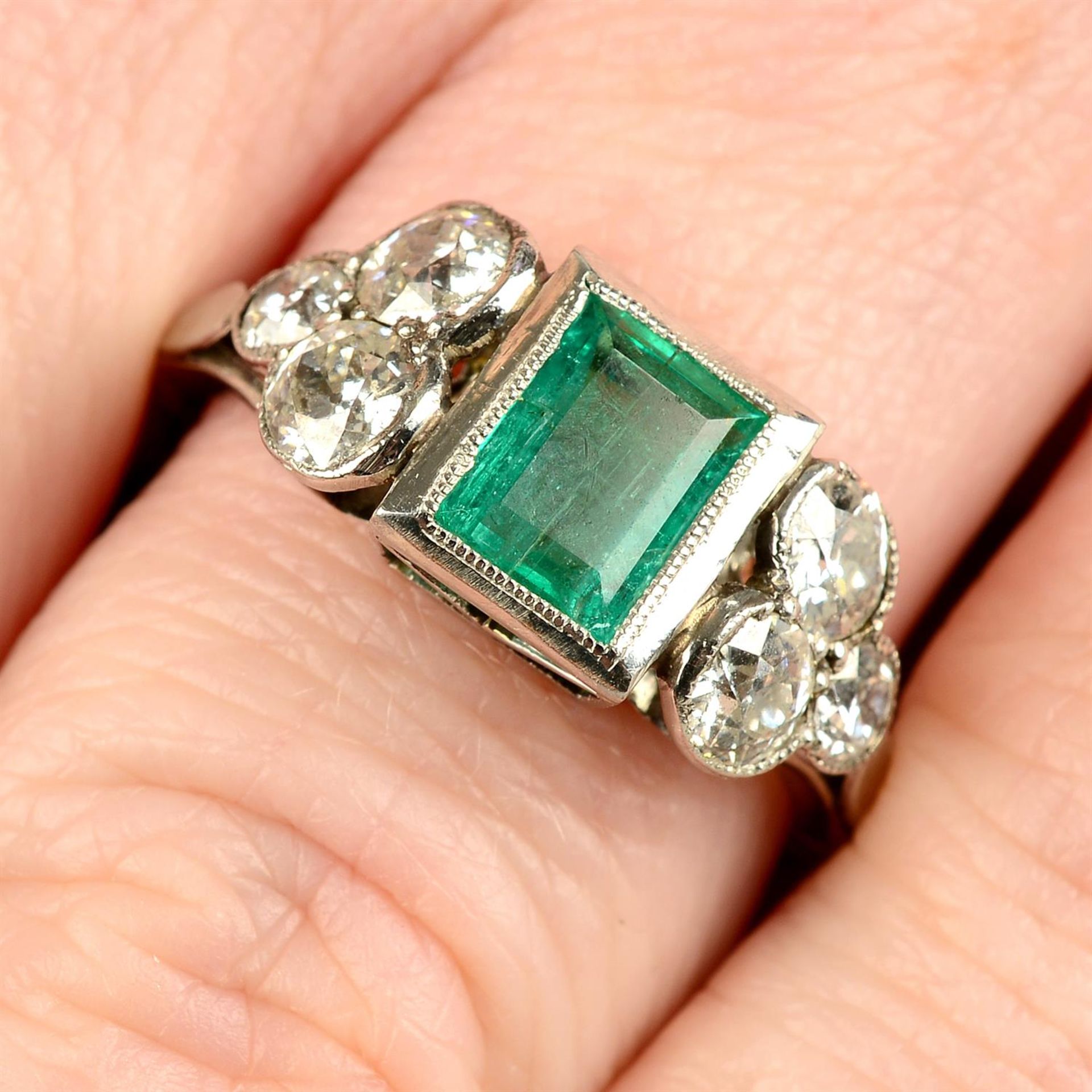 An emerald dress ring, with graduated old-cut diamond trefoil sides.