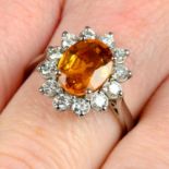 An orange sapphire and brilliant-cut diamond cluster ring.