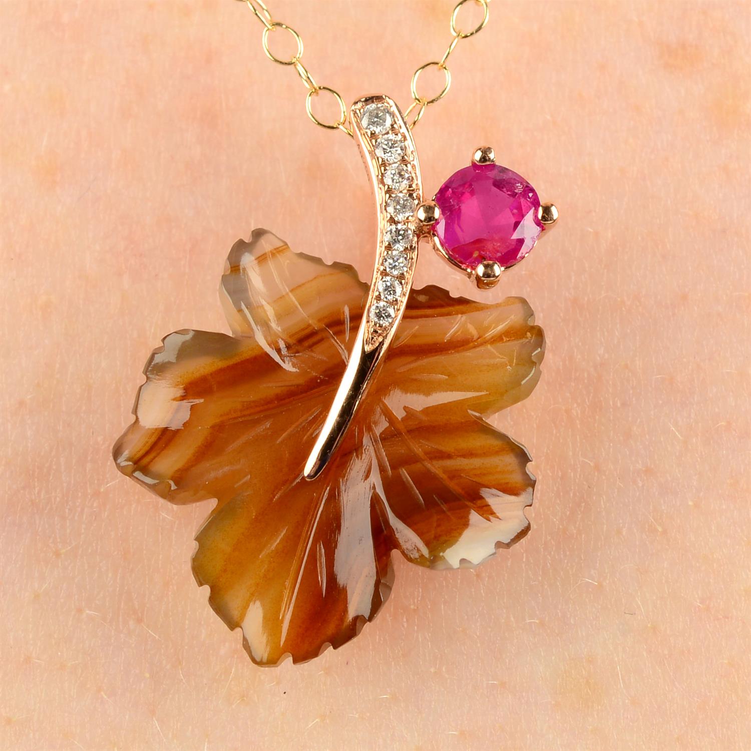 A carved foliate agate pendant, with diamond stem and ruby bud, with chain.