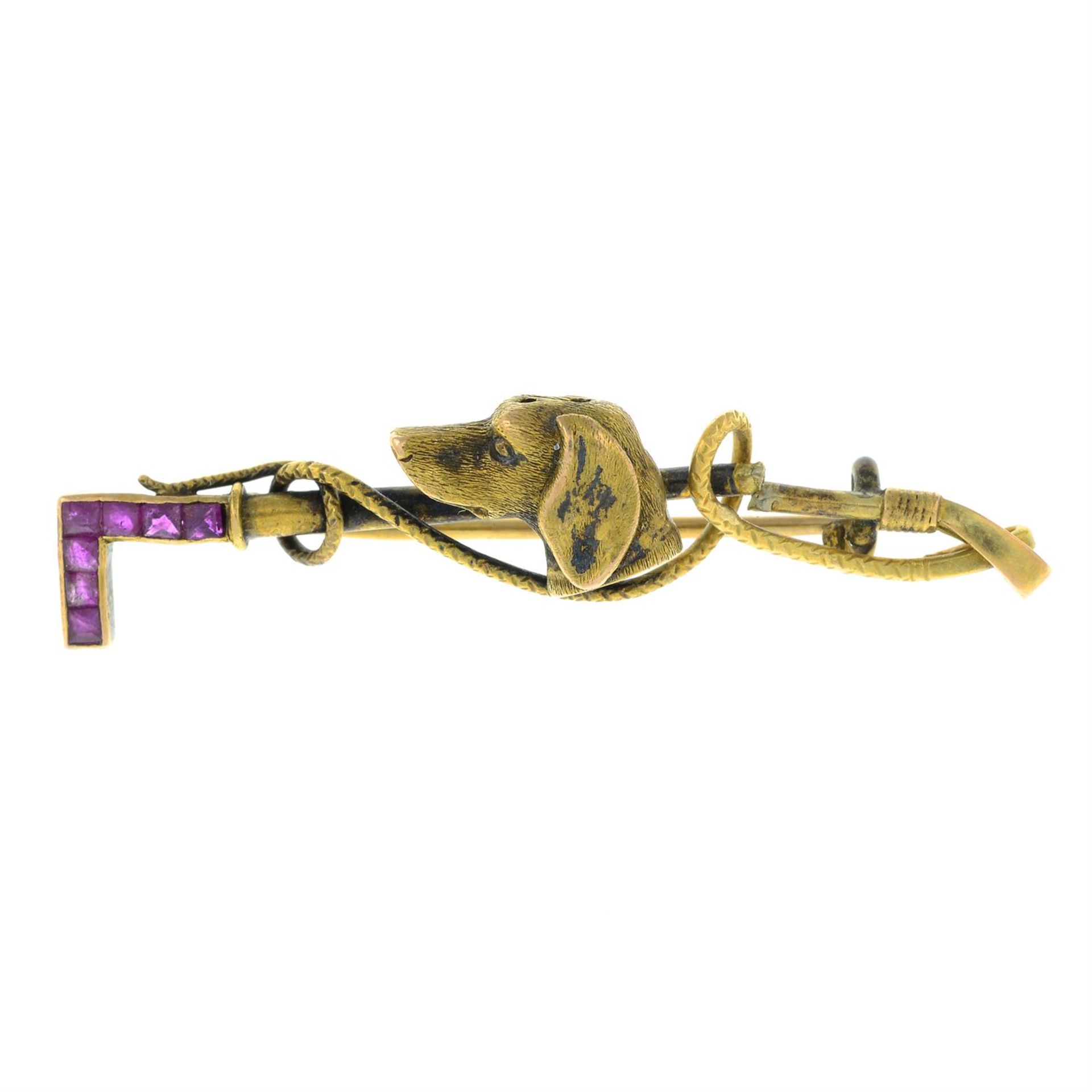 An early 20th century gold calibre-cut ruby hunting dog and riding crop bar brooch.