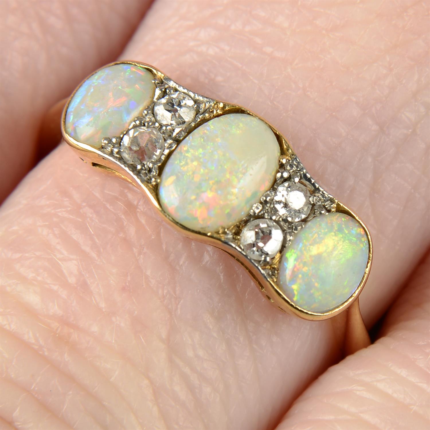 An early 20th century 18ct gold graduated opal three-stone ring, with single-cut diamond spacers.