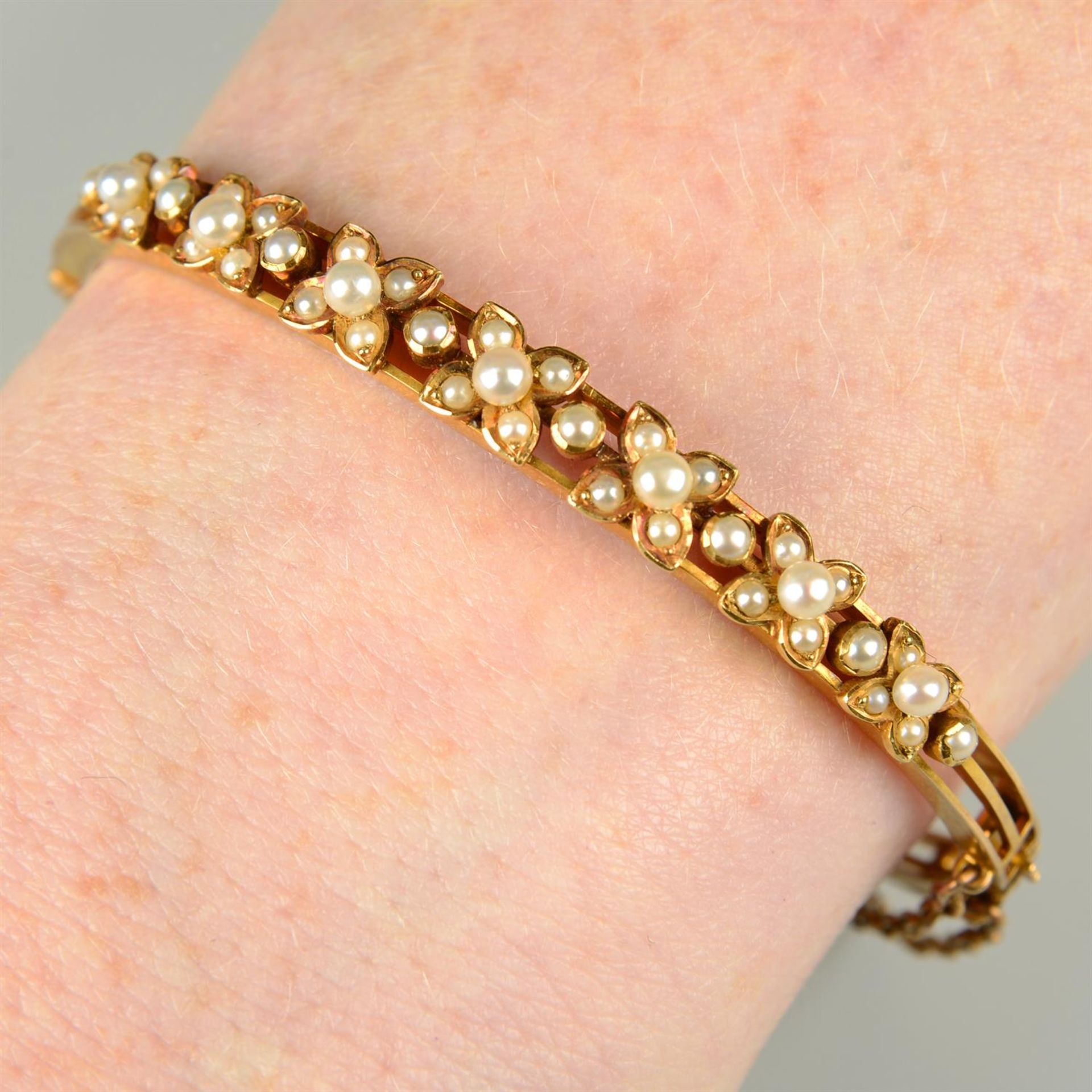 A late Victorian gold seed and split pearl floral hinged bangle.