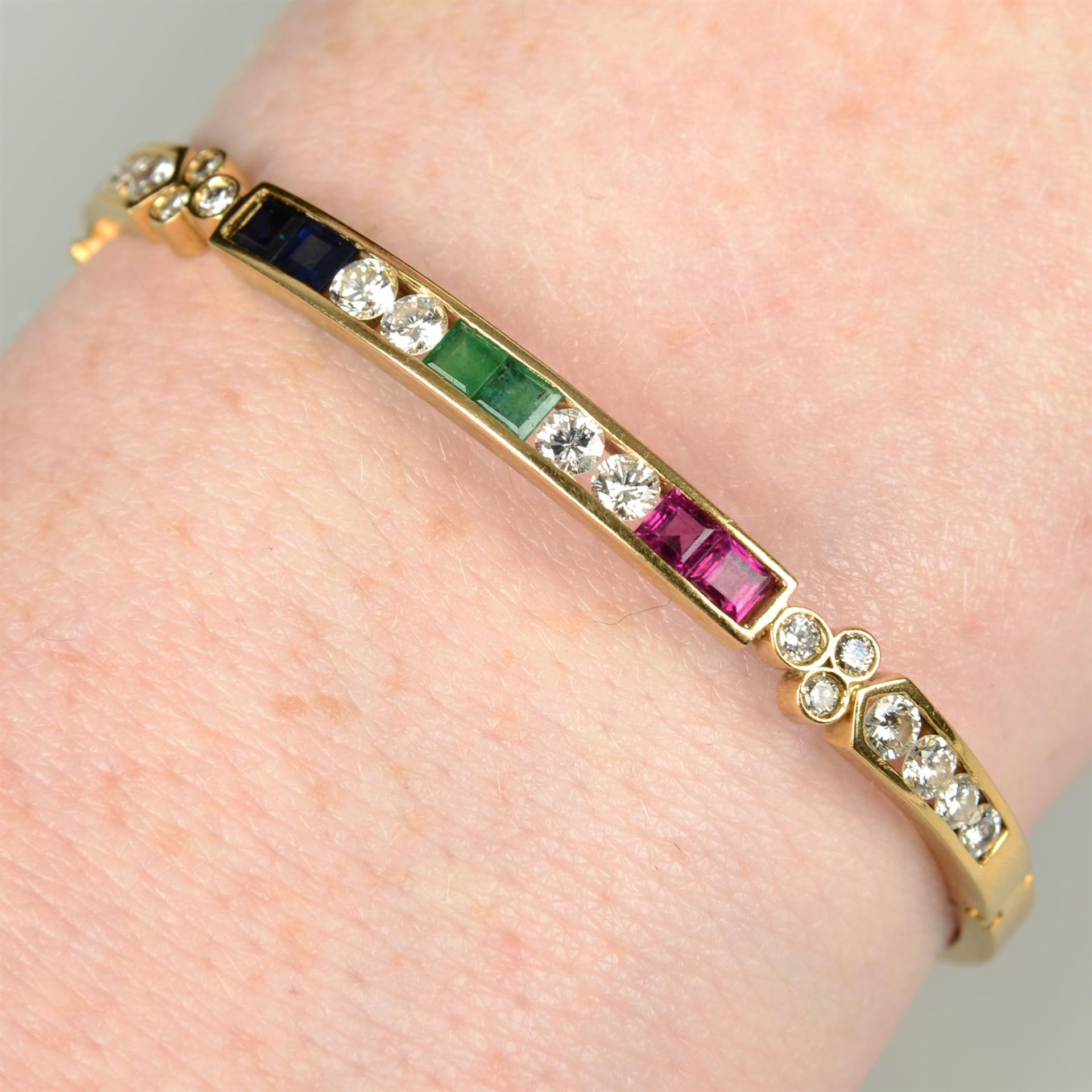 An 18ct gold brilliant-cut diamond, sapphire, emerald and ruby hinged bangle.