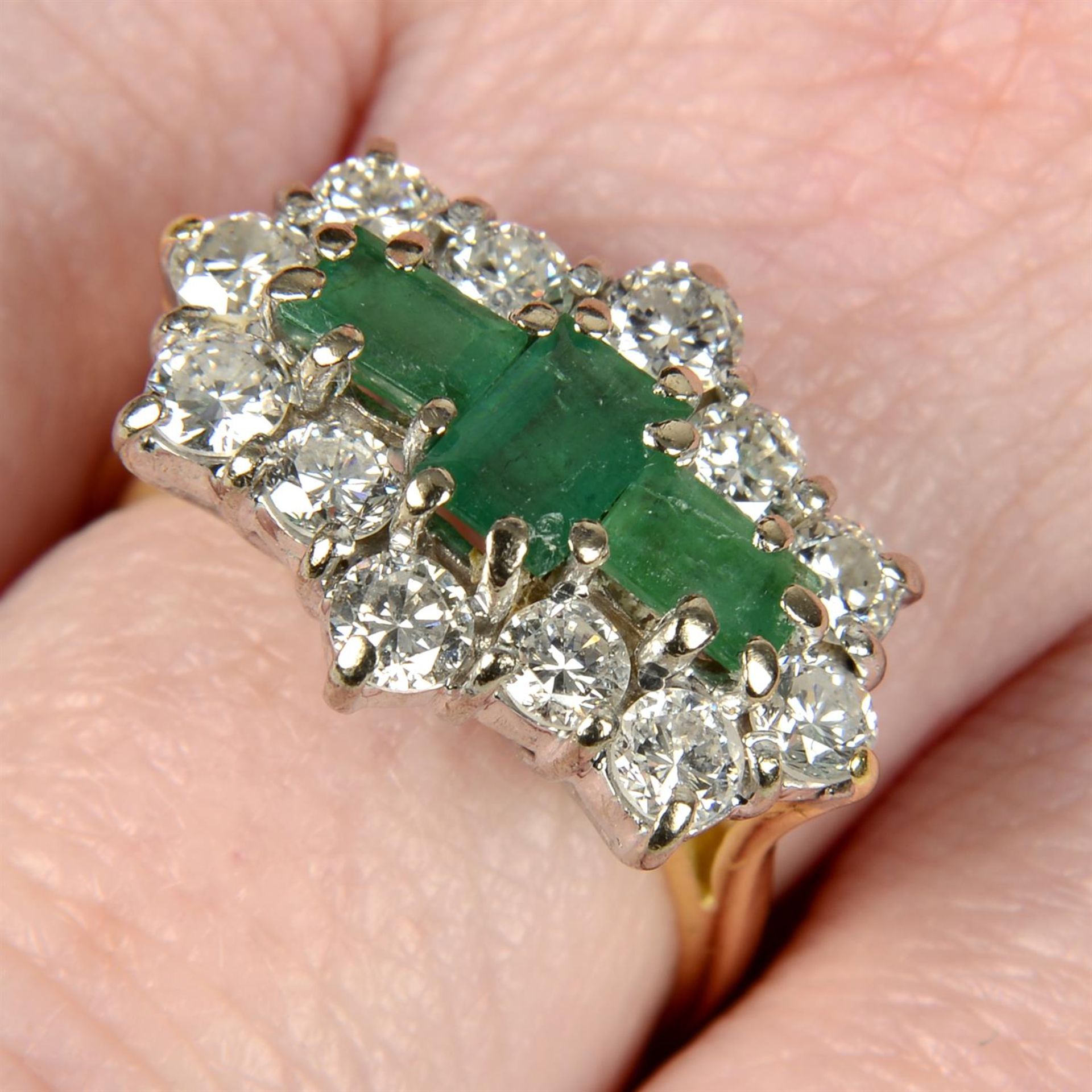 An 18ct gold emerald three-stone and brilliant-cut diamond cluster ring.