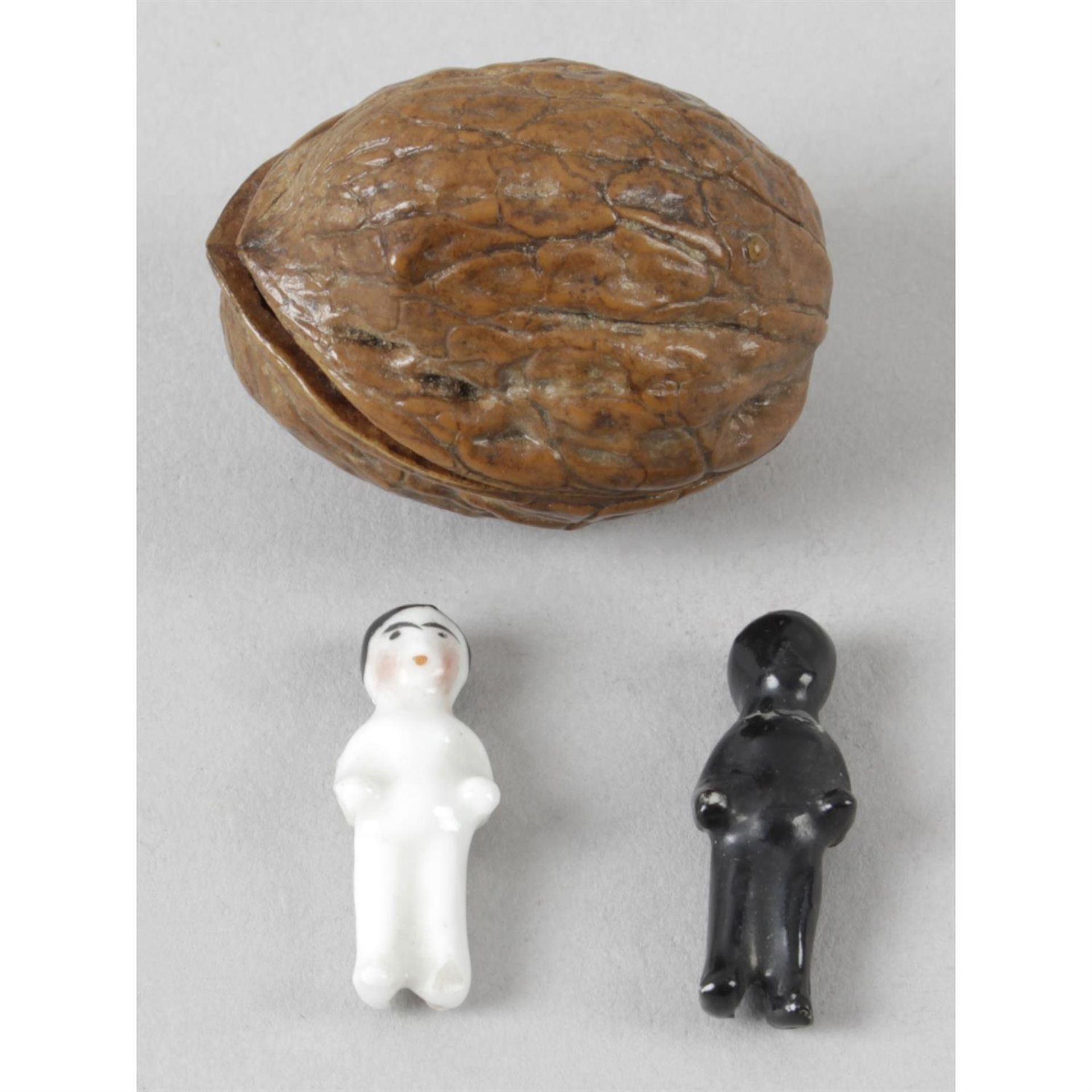 An antique walnut shell, containing two miniature ceramic dolls.