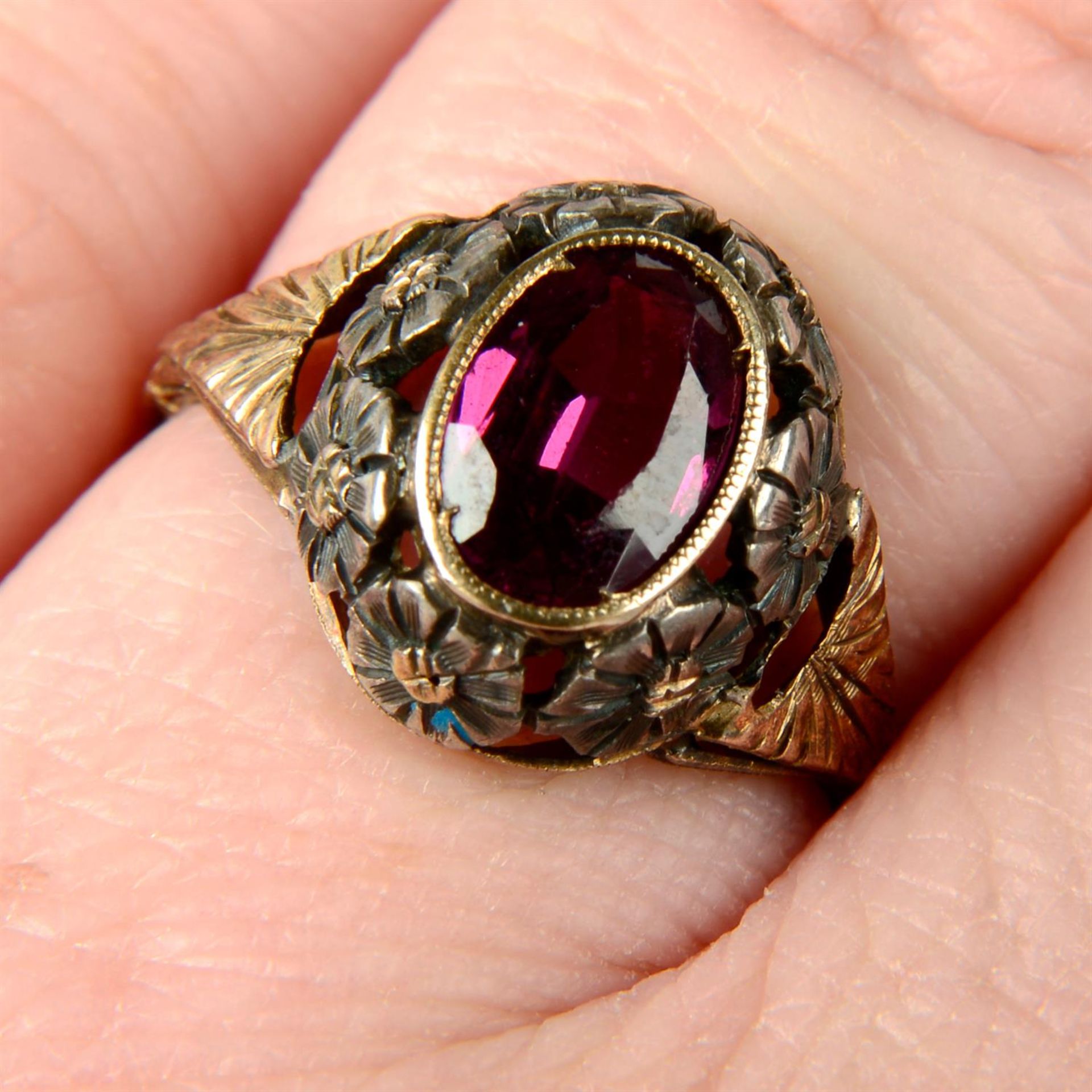 An early 20th century silver and 15ct gold garnet dress ring, with pierced floral surround.