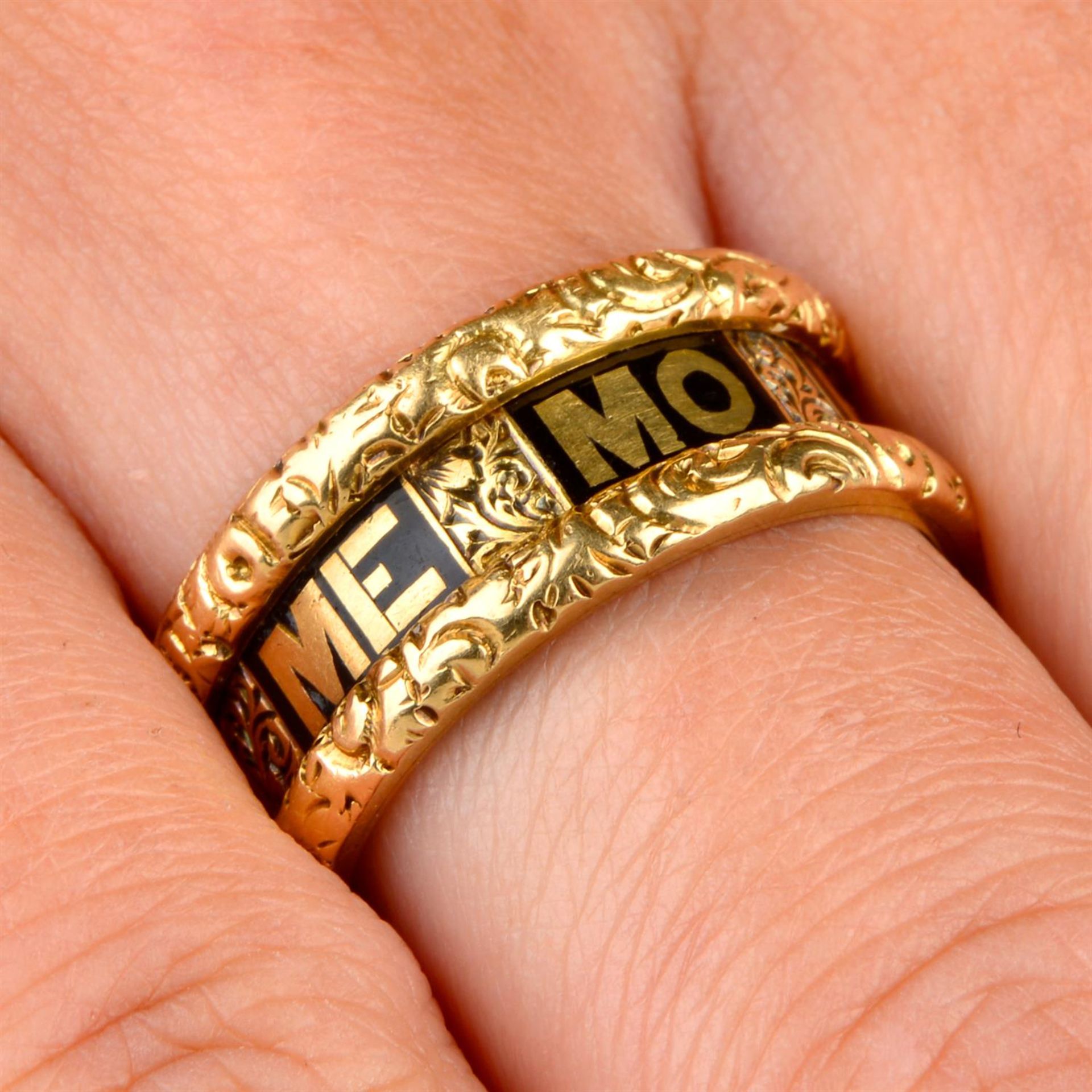 A late Victorian 18ct gold mourning ring, with black enamel 'In Memory Of' script and floral border.