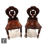 A pair of Victorian mahogany hall chairs, the pierced shield backs over serpentine seats on turned