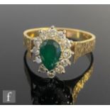 An 18ct emerald and diamond cluster ring, central pear shaped emerald within a border of twelve