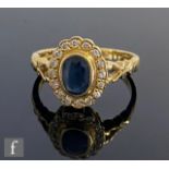 An 18ct sapphire and diamond cluster ring, central collar set oval sapphire within a border of