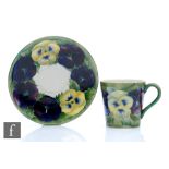 William Moorcroft - A coffee cup and saucer decorated in the Pansy pattern with purple and yellow