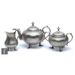 An early 20th Century white metal three piece tea set with foliate decoration and each terminating