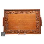 A carved wooden tray in the Arts and Crafts style with a band of stylised leaves and berries, 58cm x