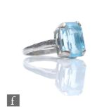 An 18ct white gold single stone aquamarine ring, claw set emerald cut stone to scrolled shoulders,