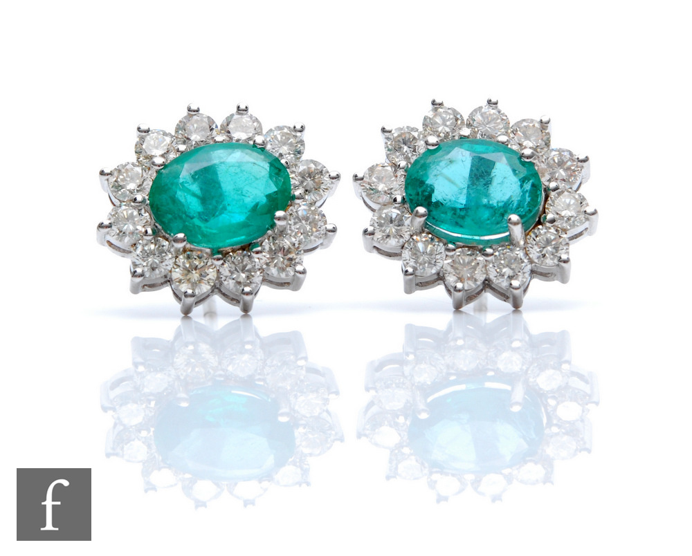A pair of 18ct white gold, emerald and diamond cluster stud earrings, each with central oval