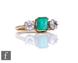 An 18ct emerald and diamond three stone ring, square cut claw set emerald flanked by a 0.40ct