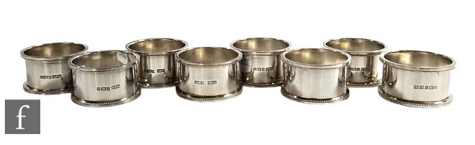 A set of eight hallmarked silver circular napkin rings of plain form terminating in beaded