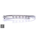 An 18ct hallmarked white gold hinged bangle, part channel set with six brilliant cut diamonds, total