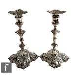 A composed pair of hallmarked silver candlesticks each with shaped square bases below knopped