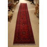 A very long burgundy ground Afghan Runner, a row of varied medallions inside a conforming border,