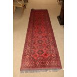 A burgundy ground Afghan Runner, with a centre row of varied medallions inside conforming borders,