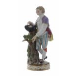 Meissen porcelain figure of a young man, standing by a tree trunk, with a small basket of eggs in