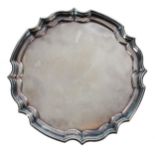 Elizabeth II circular silver card tray, with a cast stepped rim border, raised on four leaf scroll